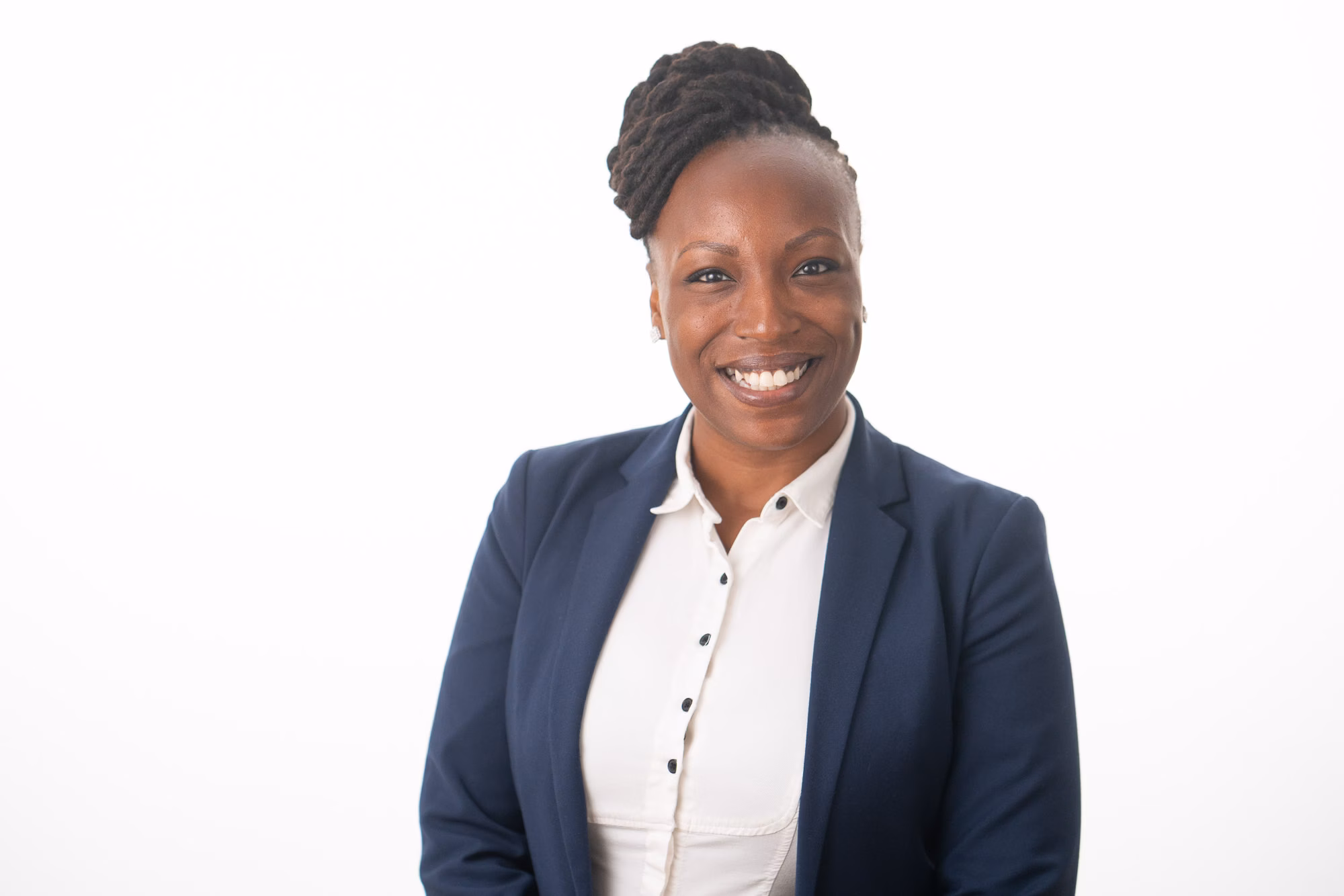 Woman in a navy blazer over a white button blouse smiles broadly against a plain white backdrop